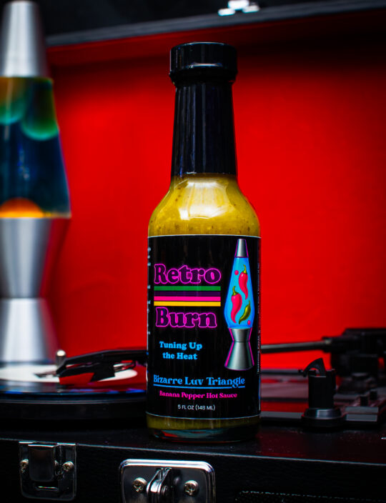 Product shot of a hot sauce on top of a vinyl player with a Lava Lamp in the Background