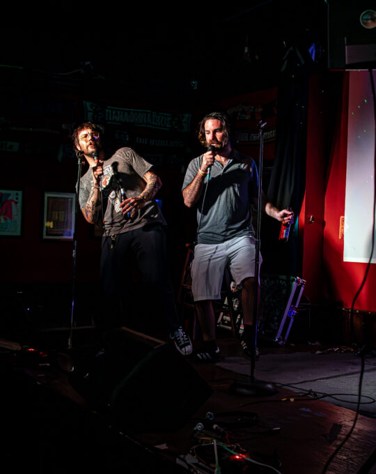 Two dudes with beers up on a stage