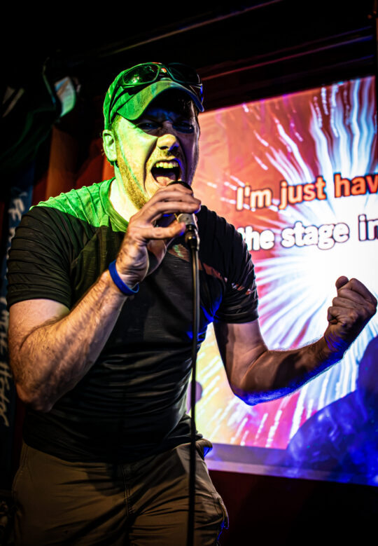 Man excited and singing karaoke into a microphone on stage with lyrics behind him
