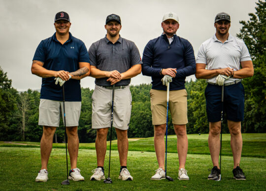 Four male golfers standing on a golf course holding their golf clubs