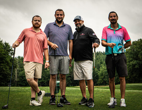 Four men on a golf course holding golf clubs with different colored shirts