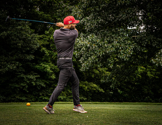 Golfer at the end of his swing with rad hat on golf course
