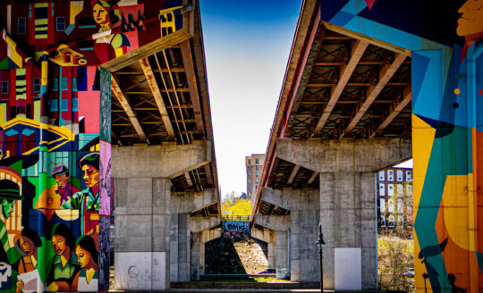 Underneath two bridges with colorful graffiti on both sides. On the left a man and on the right a bright community