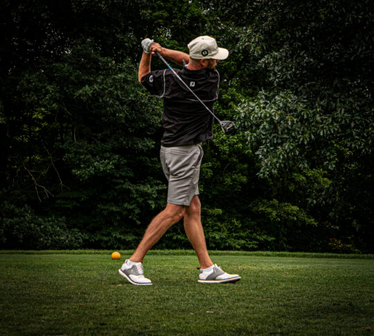 Portrait of a golfer on the follow through of hitting a golf ball on a golf course